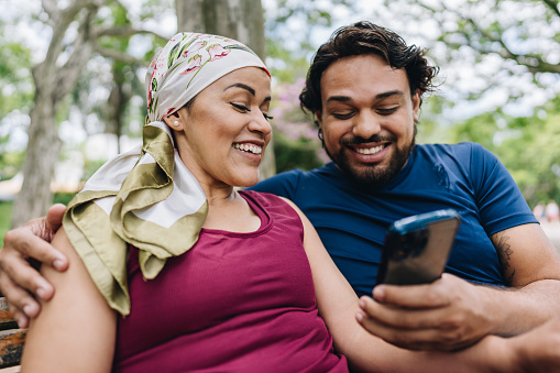 A mature woman who is battling cancer using mobile phone with her husband at park