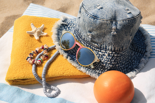 Denim hat, orange and beach accessories on sand, closeup