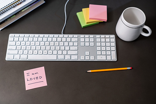 An inspirational note on a desk with keyboard, note pads, pencil, books, and coffee mug.