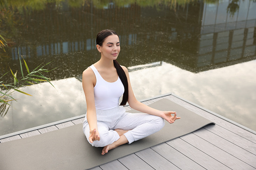 Beautiful young woman practicing Padmasana on yoga mat outdoors, above view. Lotus pose