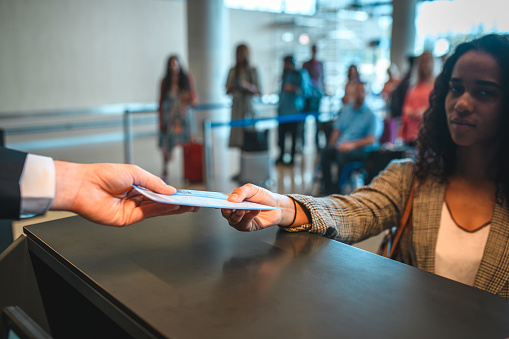 Person handing a boarding pass and a passport to a stewardess at check in counter.