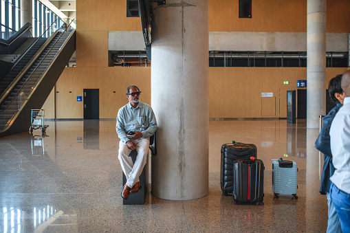 Senior Indian male sitting on a trash bin waiting for a check-in at the airport lobby.