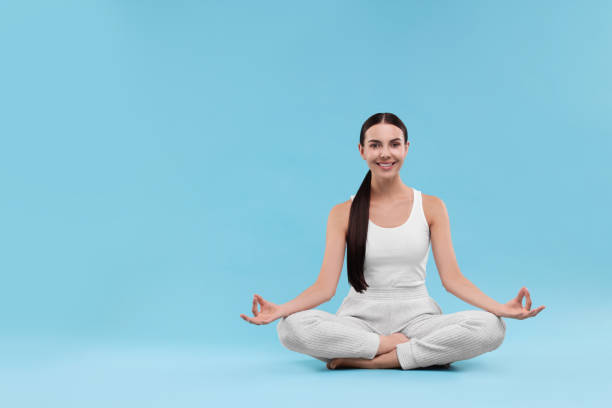 istock Beautiful young woman practicing yoga on light blue background, space for text. Lotus pose 1930048001