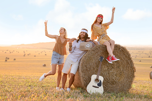 Happy hippie friends with radio receiver and guitar in field, space for text