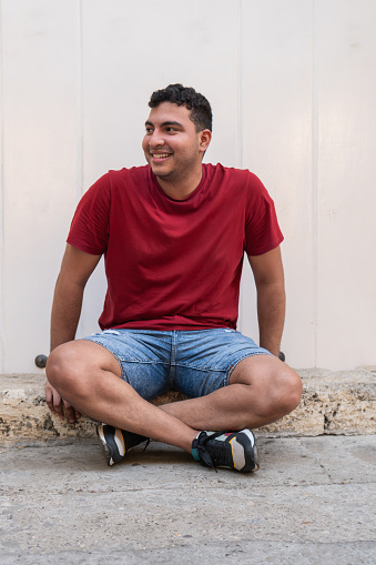 Relaxed young man with a cheerful expression sitting cross-legged against a plain white background.