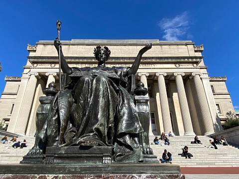 New York, NY USA - November 2, 2023 : Close-up of the bronze Alma Mater statue by Daniel Chester French in front of students sitting on the Low Library steps on Columbia University's main campus on a sunny day in Morningside Heights, NYC
