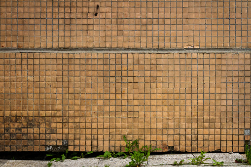 Old beige small tile wall and a sidewalk.