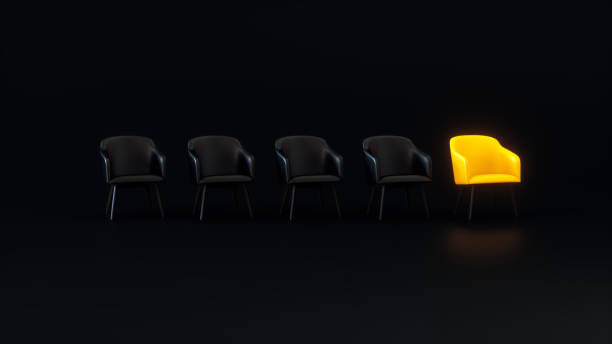 istock A Yellow Glowing Chair That Stands Out From the Black Chairs Crowd on a Dark Studio Background. Business concept. 1930125062