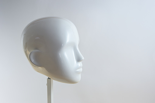 White neutral head of a mannequin figure in minimalist style on a metal stand against a light beige gray background, copy space, selected focus