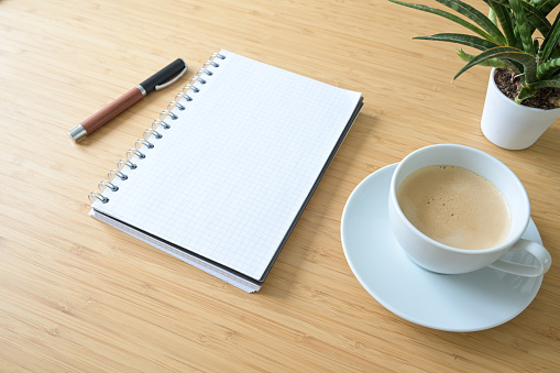 Blank spiral notepad, coffee cup, pen and a plant on a desk made of bamboo wood, business or home office concept, mockup, copy space, selected focus, very narrow depth of field