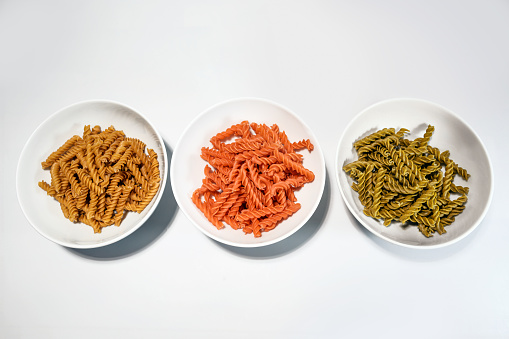 Legume pasta fusilli with less carbohydrates but more protein and fiber for a healthy diet, made from chickpeas, red lentils and mung beans in three white bowls, top view, copy space, selected focus