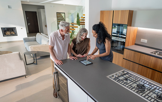 Female real estate agent showing property for sale catalog on digital tablet to buyers couple. Luxury lifestyle and new beginning concept.