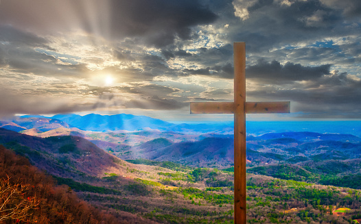 Sunrays illuminate the hills valleys behind an old wooden cross.