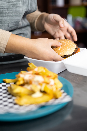 packing a hamburger and fries in a container for delivery, fast and unhealthy food, work and business