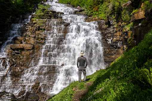 Man, hiker, standing on a trail watching a cascading waterfall over many short steps, Florence Falls, Glacier National Park, Montana