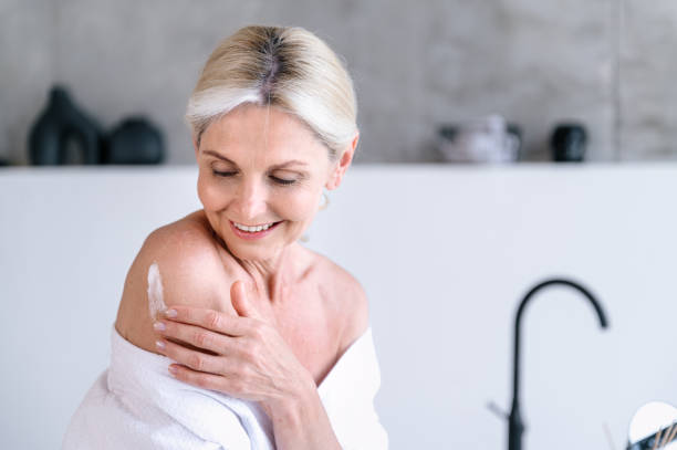 istock Middle age female smiling, applying cream on naked shoulder 1930214024