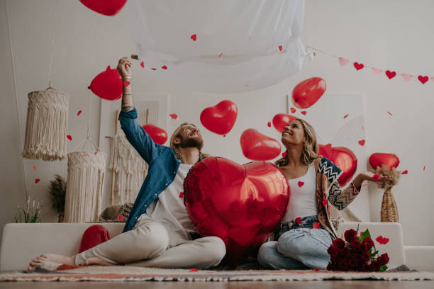 istock Smiling couple holding red heart shape balloon and throwing confetti while celebrating Valentines day at home 1930219298