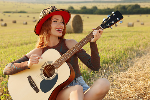 Beautiful happy hippie woman playing guitar in field