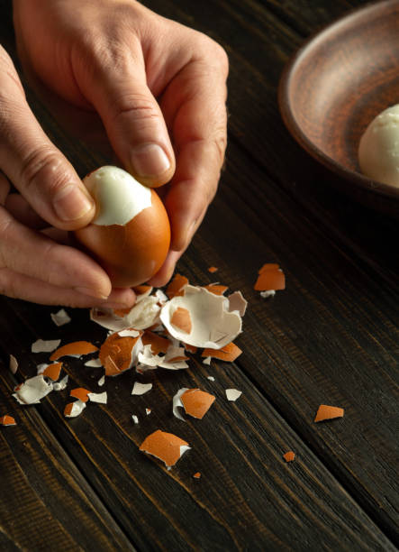 istock Close-up of a man hands peeling a boiled egg on a kitchen black table for a snack. Dark space for inscription. 1930219313