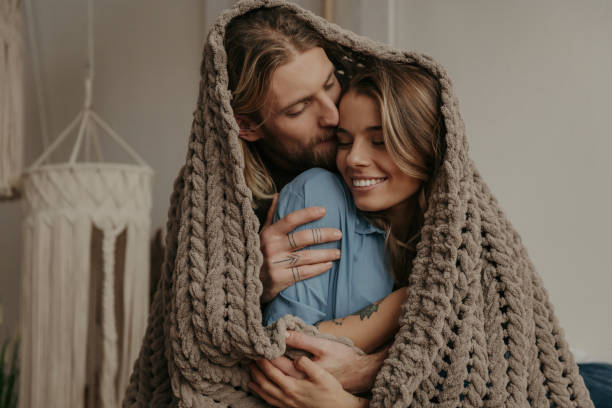 istock Young loving couple covering with a cozy warm blanket while spending romantic time at home together 1930236465