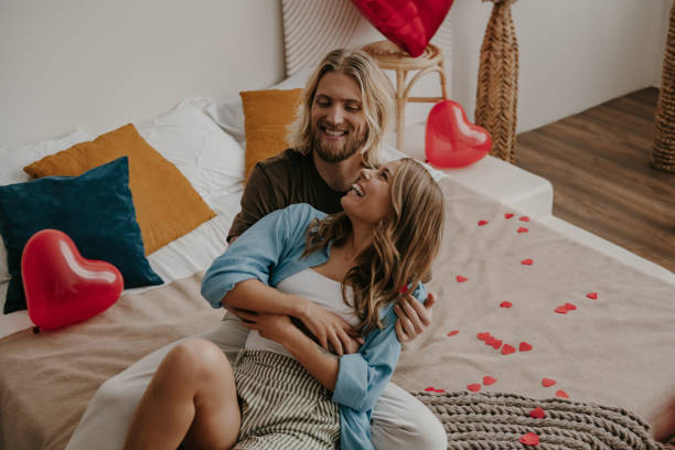 istock Happy loving couple embracing and having fun while sitting on bed surrounded with red heart shape balloons 1930236984