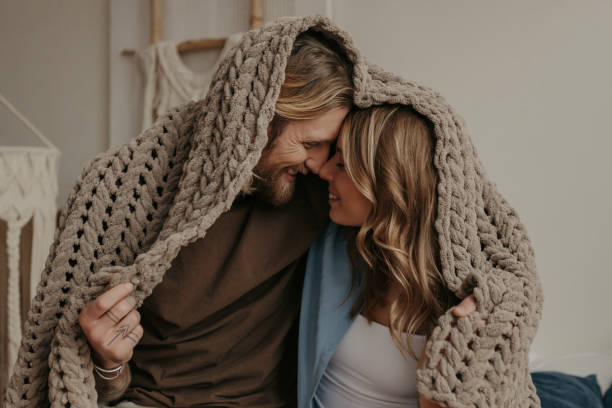 istock Joyful young loving couple covered with a cozy warm blanket smiling while sitting on bed together 1930240157