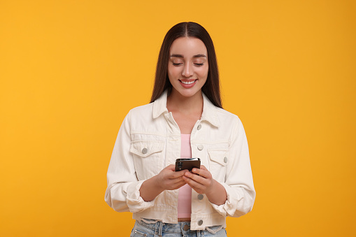 Happy young woman using smartphone on yellow background
