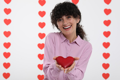 Happy young woman holding decorative red heart on decorated background