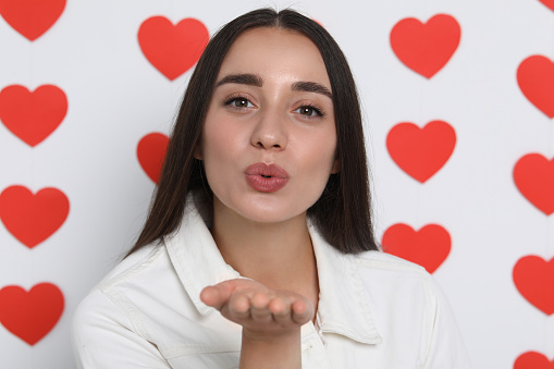 Young woman blowing kiss into camera on decorated background