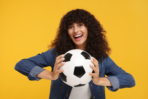 Excited fan holding soccer ball on yellow background