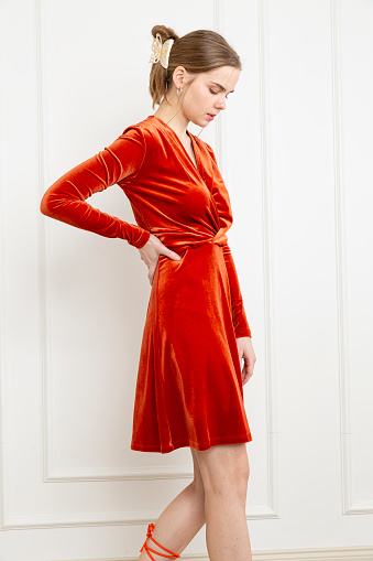 Blonde young woman wearing orange dress. Long sleeve velvet dress. Orange high heels.
