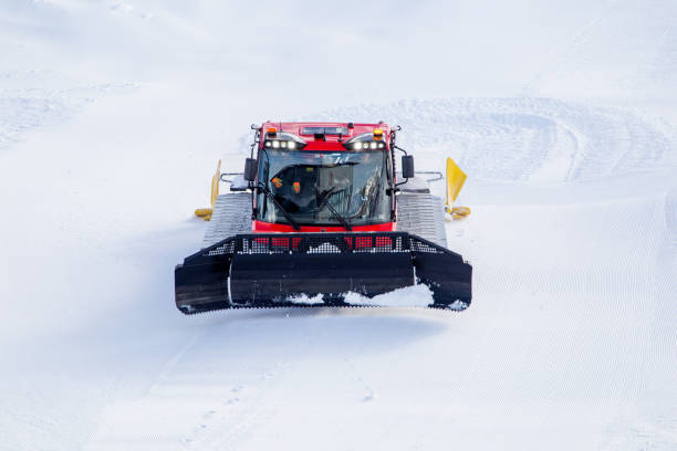 Snow groomers working on ski slopes during a foggy morning. The lights of the vehicles shine through the mist as they level and prepare the snow for skiing. The scene depicts the dedication to mountain maintenance and preparation for winter sports enthusiasts. A peaceful and atmospheric moment in a winter resort.