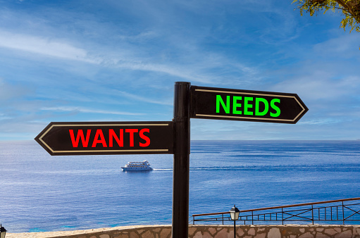 Needs or wants symbol. Concept word Needs or Wants on beautiful signpost with two arrows. Beautiful blue sea sky with clouds background. Business and needs or wants concept. Copy space.