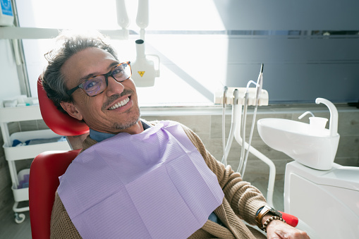 Satisfied man sitting on a dental chair smiling after a dental procedure