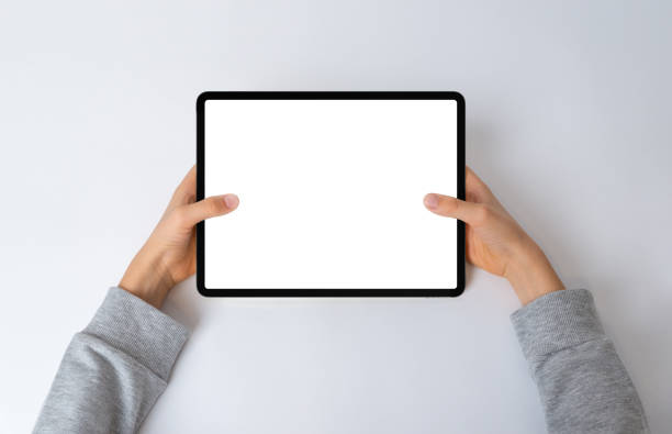 istock Top view of a kid's hands holding a horizontal tablet on a desk. Flat lay composition with an isolated screen for mockup, perfect for showcasing interactive content 1930399475