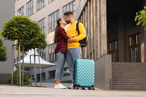 Long-distance relationship. Beautiful couple with luggage kissing outdoors, low angle view
