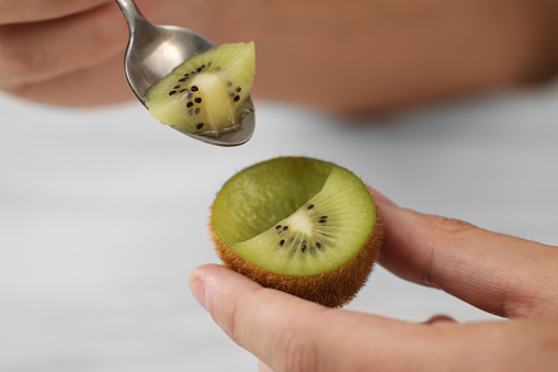 Man eating kiwi with spoon on blurred background, closeup