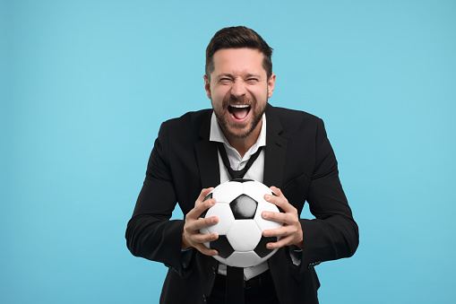 Emotional sports fan with ball celebrating on light blue background