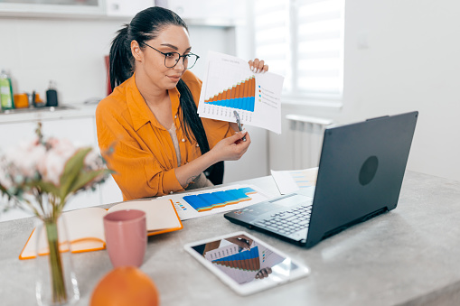 A young adult female, viewed from the front, is writing a to-do list while working on her laptop at home, highlighting the disciplined approach of freelance professionals