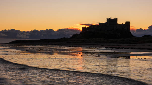beautiful landscape image of northumberland beach in northern england during winter dawn with deep orange sky - bamburgh northumberland england beach cloud foto e immagini stock