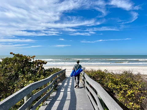 Active senior man carries beach chairs as he crosses the access foot bridge to Indian Rocks Beach in Florida on the gulf coast.