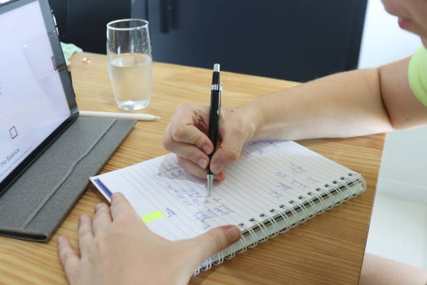 istock Woman writing in her notebook with a sharp pencil. Wooden table with tablet and notebook beeing used for study. 1930590363