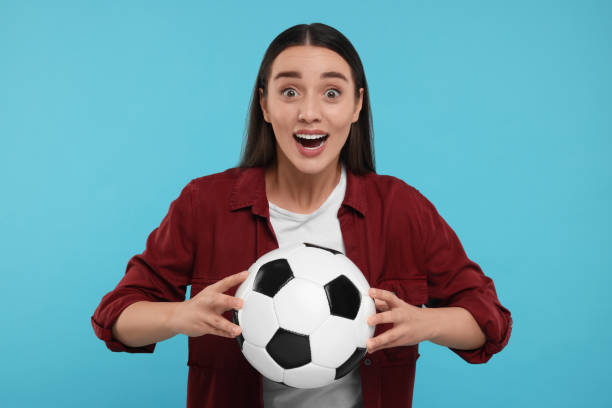 istock Surprised fan holding soccer ball on light blue background 1930590915