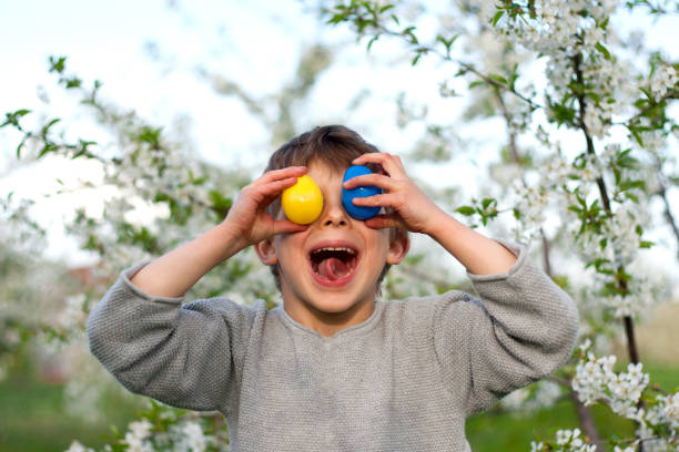 Happy easter. Cute funny preschooler boy with Easter eggs in garden, portrait against background of blooming tree. Laughing child during an Easter egg hunt. Holiday tradition. Spring, outdoor