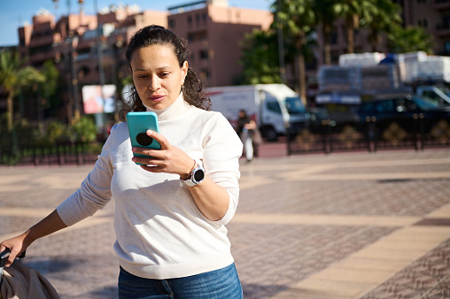Young woman checking smart phone on the street, online shopping, booking taxi, ordering, searching geolocation on online maps on mobile application. People. Internet communication. Wireless technology