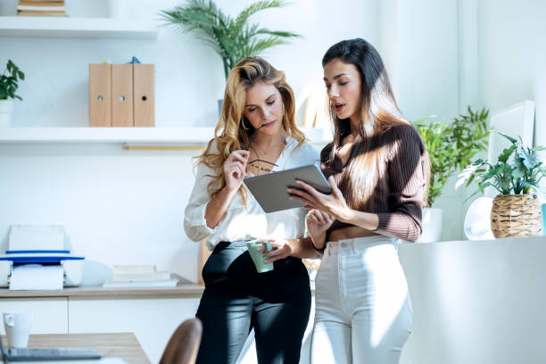 istock Two attractive young business women working with the digital tablet while talking in a modern office 1930807142