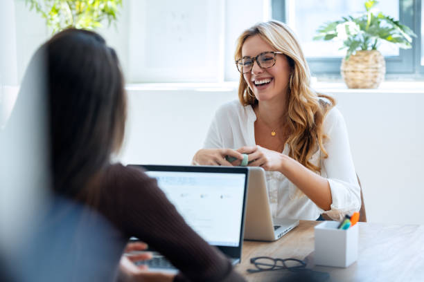istock Two elegant attractive businesswomen talking while working together with laptop in a modern startup 1930810752