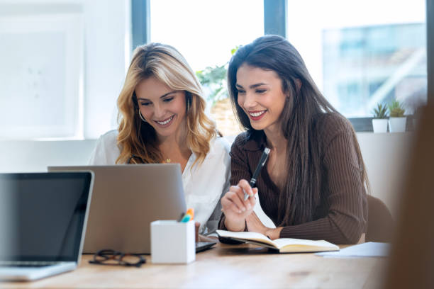 istock Two elegant attractive businesswomen talking while working together with laptop in a modern startup 1930811793