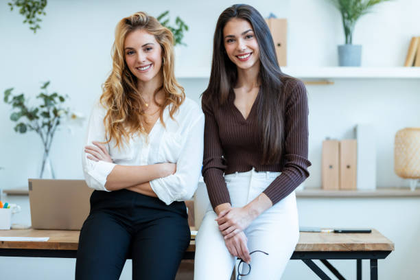 istock Two elegant attractive businesswomen working while looking at camera in a modern startup 1930812849