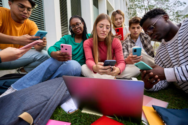 group of young multiracial university students immersed on their mobile cell technology addicted - multi ethnic group concentration mobile phone using laptop imagens e fotografias de stock